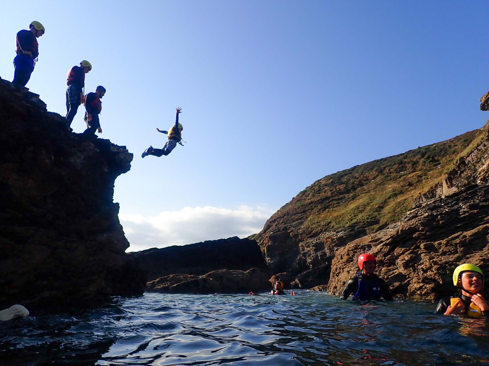 Participants coasteering at Praa Sands, West Cornwall, with a guided cliff jump into the sea during a session run by Kernow Coasteering